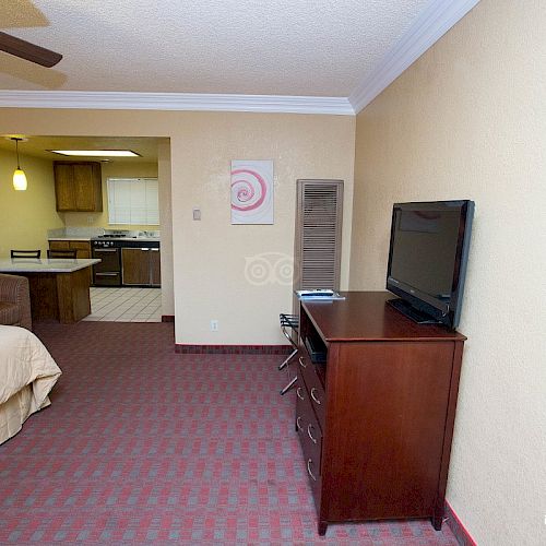 A hotel room with a bed, TV on a dresser, and a kitchenette area in the background, with warm lighting and simple decor, seen from tripadvisor.